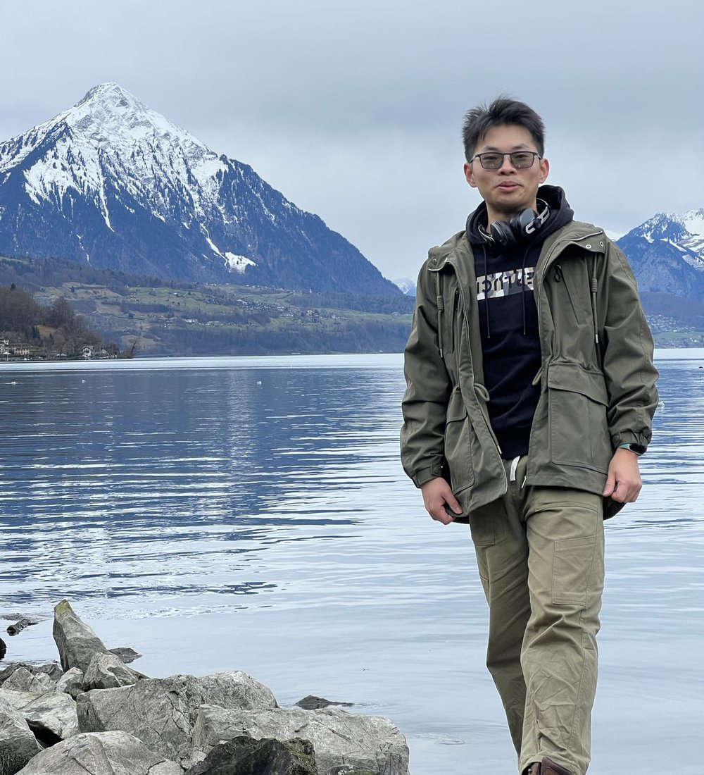 Fengyun Yu standing by a lake with snow-capped mountains behind